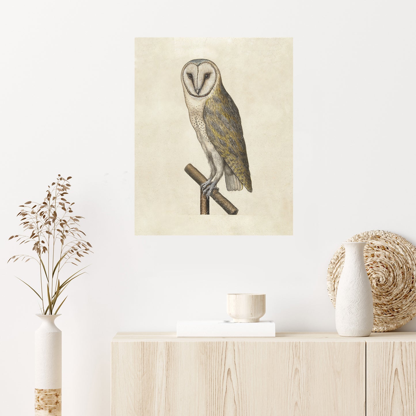 A minimalist interior features "Night Owl," a vintage-style illustration of a barn owl perched on a branch. Below the artwork, a light wooden sideboard holds a small bowl, a decorative vase with dried botanicals, and a woven basket.