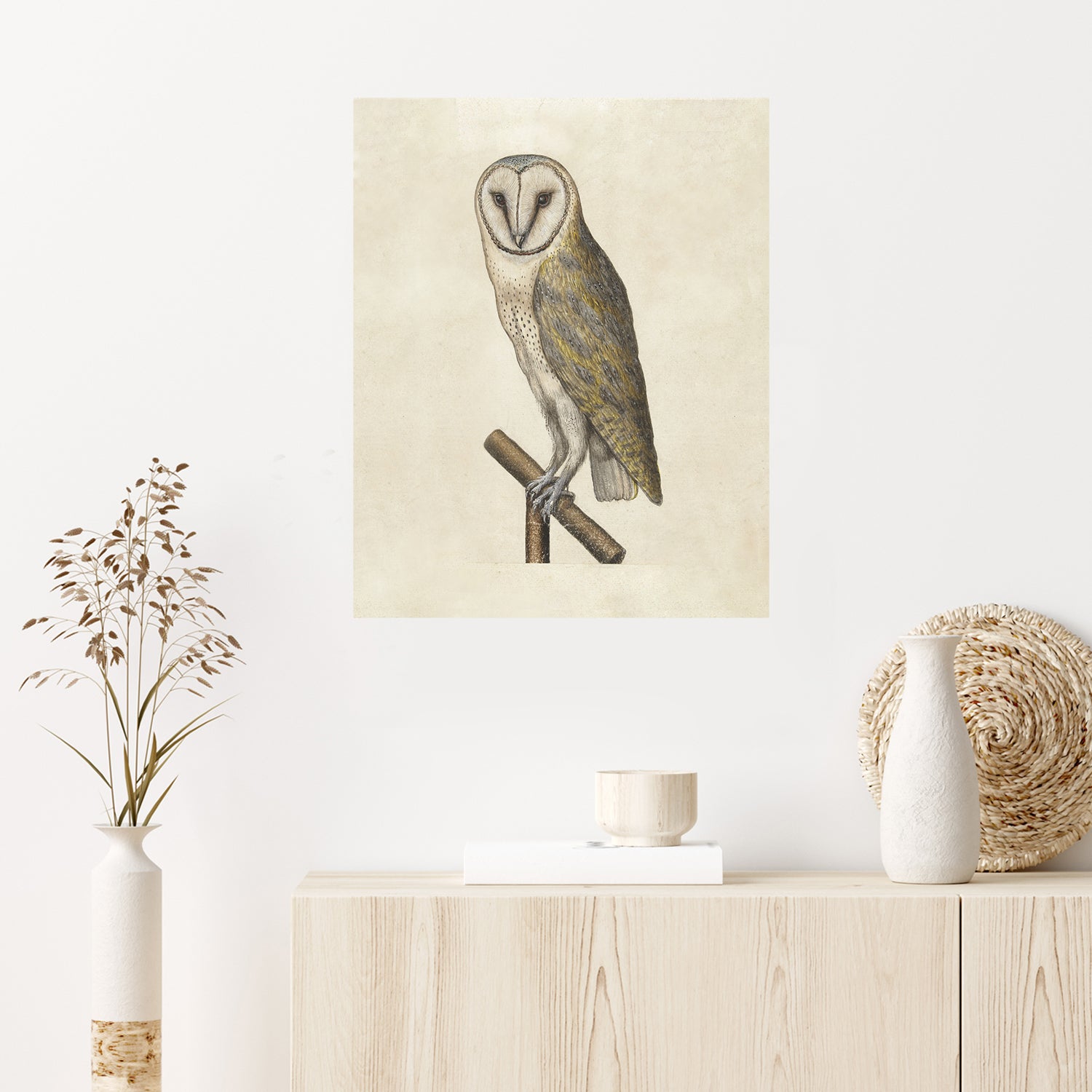 A minimalist interior features "Night Owl," a vintage-style illustration of a barn owl perched on a branch. Below the artwork, a light wooden sideboard holds a small bowl, a decorative vase with dried botanicals, and a woven basket.
