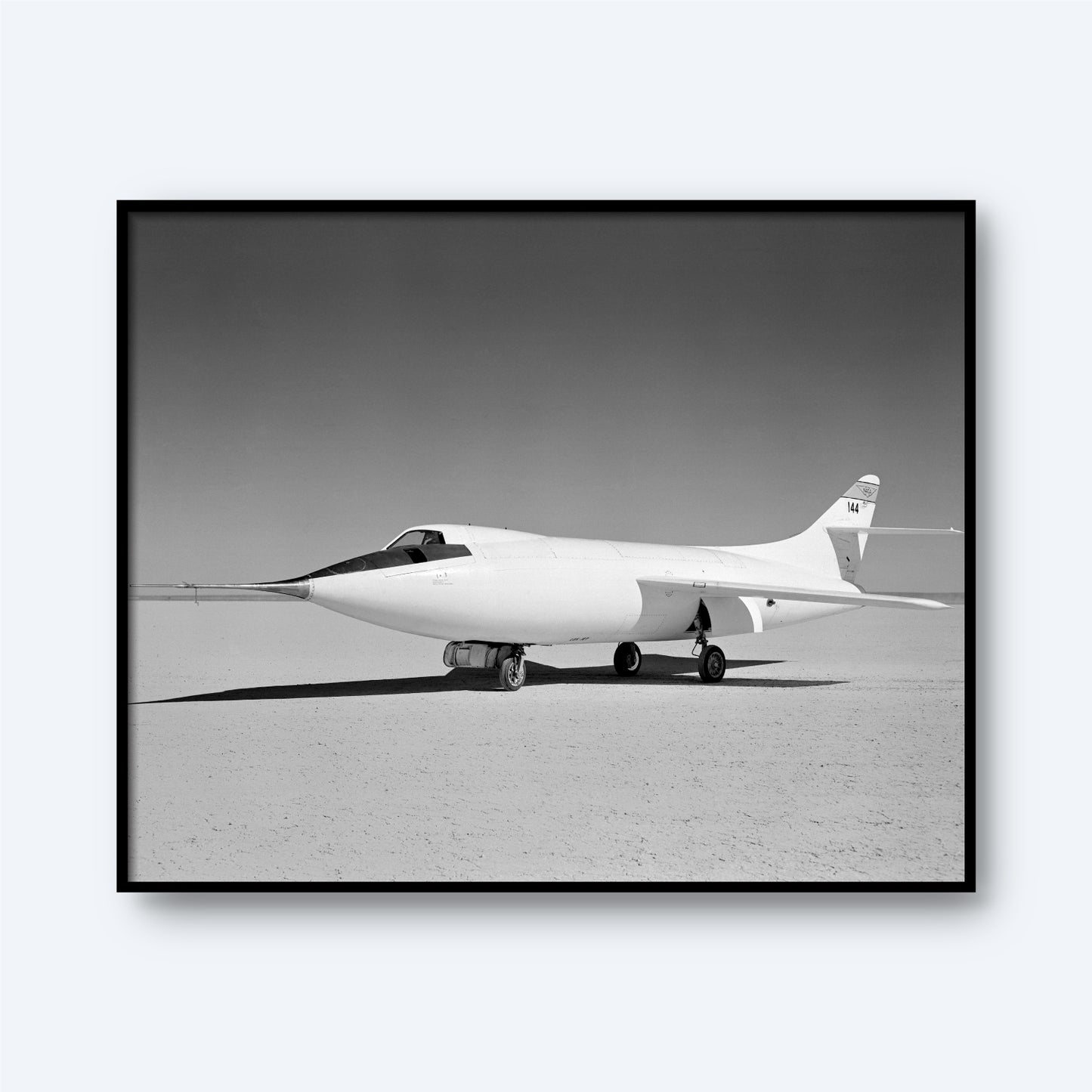 A black and white photo showcases the D-558-II Skyrocket Aircraft | X Planes, a marvel in aviation history, parked on a flat, barren expanse. The sleek, streamlined aircraft, with no visible markings on its fuselage and a single tail fin, is illuminated by sunlight under a clear sky—an emblem of the supersonic flight era.
