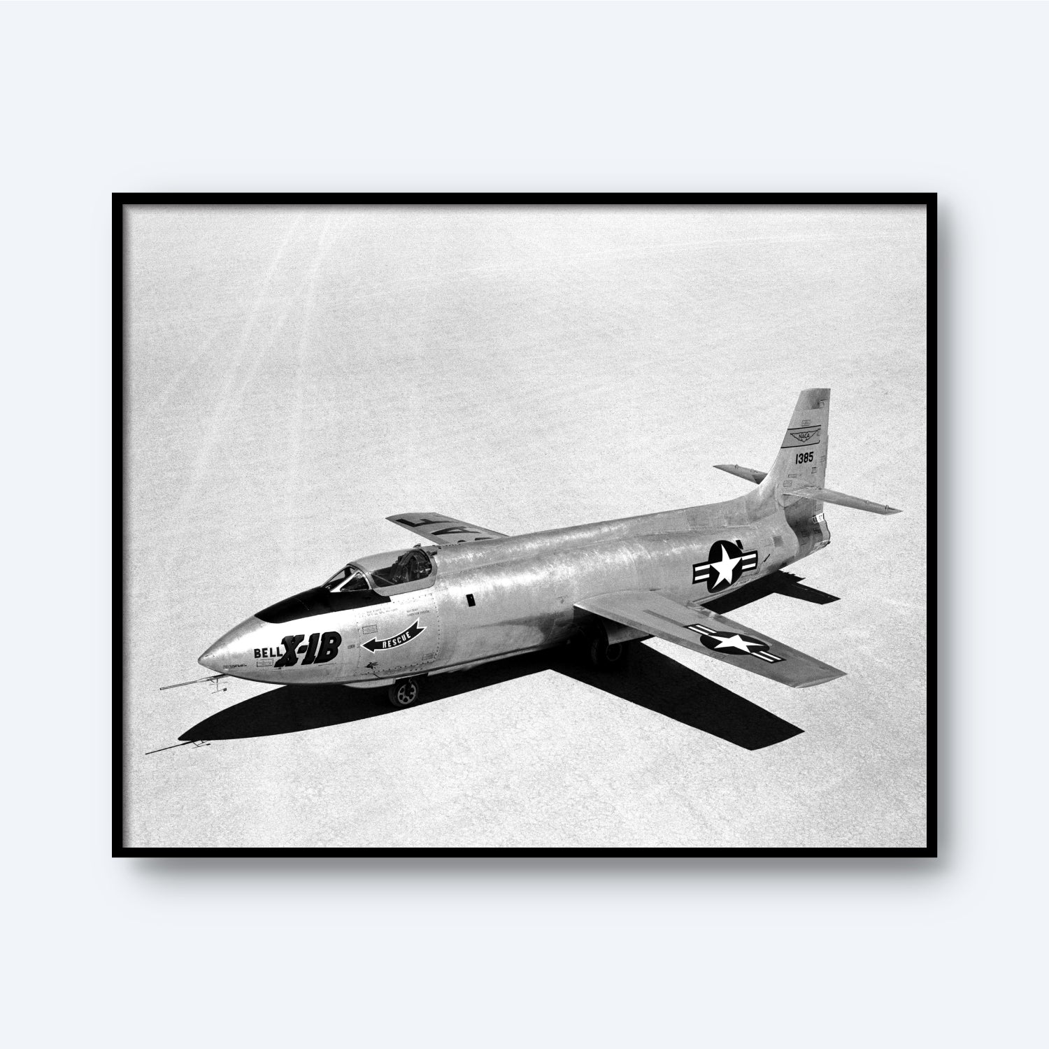 A black and white photo, titled "X-1B on Lakebed | X Planes," showcases the experimental X-1B aircraft on a flat, open surface. The sleek airplane, vital in aerospace history, features a rounded nose and wings adorned with U.S. Air Force insignia clearly visible on the sides and wings. The aircraft is positioned diagonally in the frame.