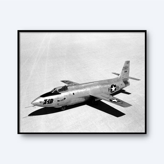 A black and white photo, titled "X-1B on Lakebed | X Planes," showcases the experimental X-1B aircraft on a flat, open surface. The sleek airplane, vital in aerospace history, features a rounded nose and wings adorned with U.S. Air Force insignia clearly visible on the sides and wings. The aircraft is positioned diagonally in the frame.