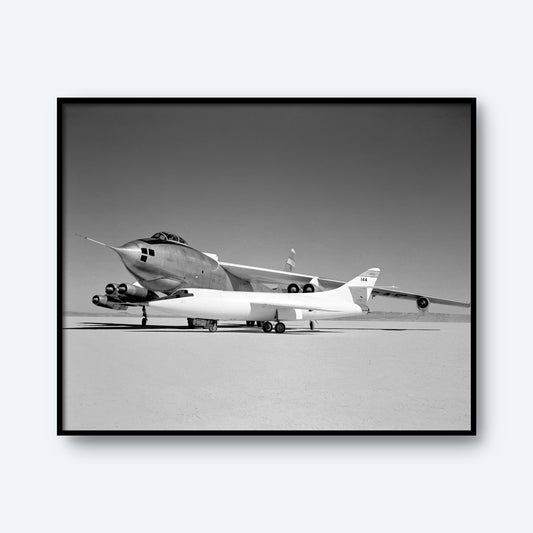Monochromatic image capturing a significant moment in aviation history, featuring a large Boeing B-47A Stratojet with a smaller Douglas D-558-II attached beneath its fuselage. The aircraft are stationary on a dry, flat surface reminiscent of a desert or test area, emphasizing their sleek and sharp-nosed design. This print is titled "Douglas D-558-II and Boeing B-47A Stratojet Print | X Planes.