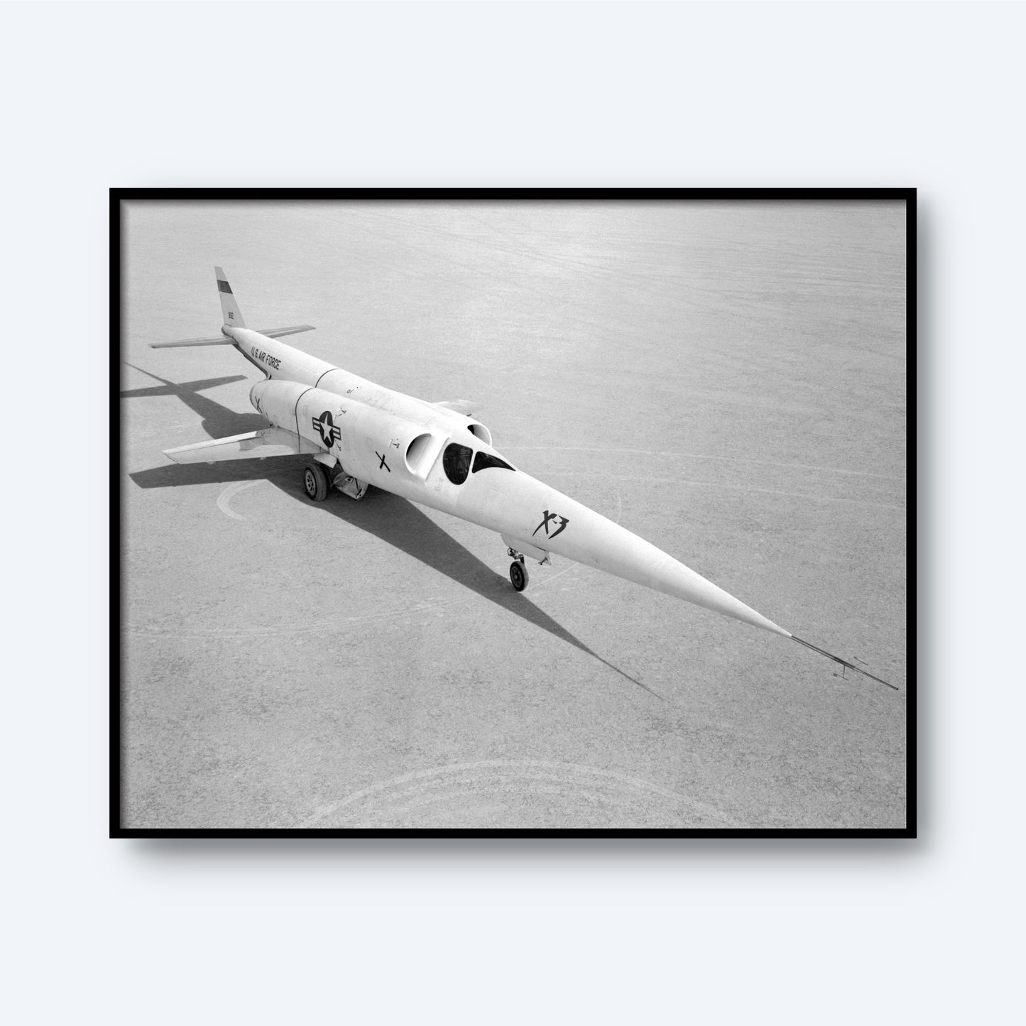 A black and white image captures the sleek, experimental X-3 aircraft, characterized by its long, pointed nose and short wings, parked on a flat lakebed runway. Adorned with military insignia and the designation "X3," its shadow is clearly visible on the ground. This stunning print from 'X Planes' is perfect for aviation wall art or aerospace engineering decor.