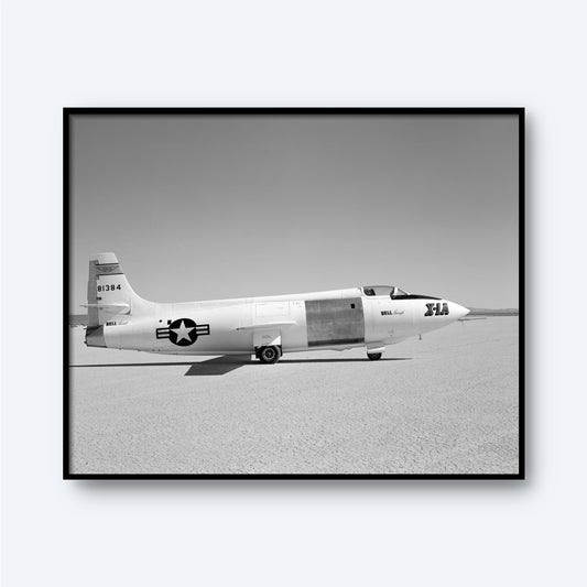 A black and white photograph of the X-1A Aircraft with Unpainted Fuselage Print from X Planes, depicting the aircraft on a flat, barren surface. The unpainted fuselage bears the number 606384 on its tail and a star emblem with stripes on its side. The text "Bell XS-1" and "the Glamorous Glennis" are visible, marking an era of supersonic flight.