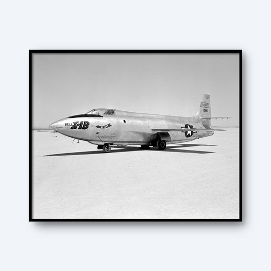 Black and white photo of the Bell Aircraft Corporation X-1B, a historic rocket-powered aircraft, stationed on the ground of a flat, open area. The sleek and pointed X-1B features "Glamorous Glennis" painted on its fuselage and "6062" on its tail, embodying aviation history.