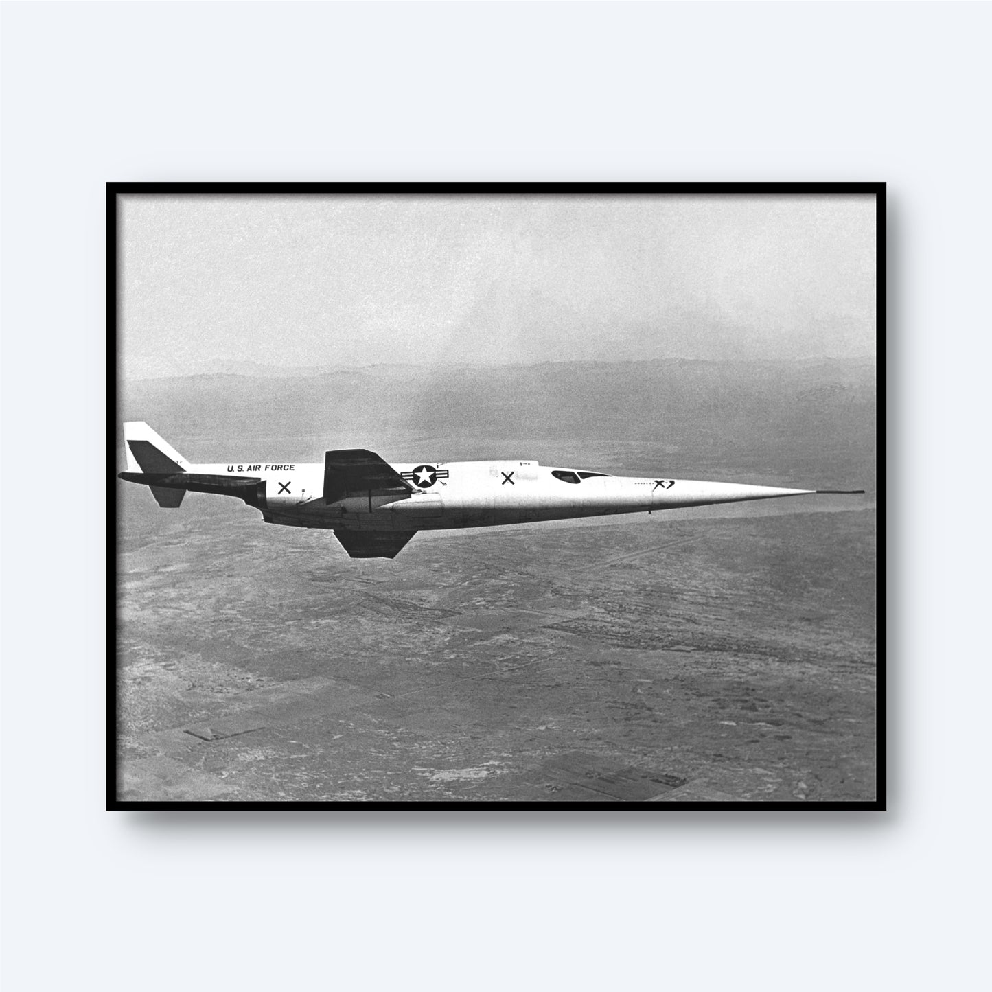 A framed black and white "In-flight Photo of the Douglas X-3" print from the X Planes collection showcases the sleek, jet-propelled experimental aircraft soaring at supersonic speeds. Adorned with "U.S. Air Force" markings and insignia on its side, the Douglas X-3 glides over a vast, indistinct landscape with a blurred horizon in this striking image.