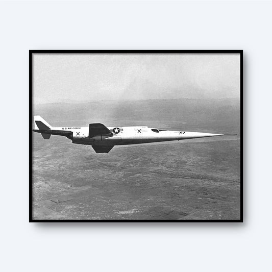 A framed black and white "In-flight Photo of the Douglas X-3" print from the X Planes collection showcases the sleek, jet-propelled experimental aircraft soaring at supersonic speeds. Adorned with "U.S. Air Force" markings and insignia on its side, the Douglas X-3 glides over a vast, indistinct landscape with a blurred horizon in this striking image.