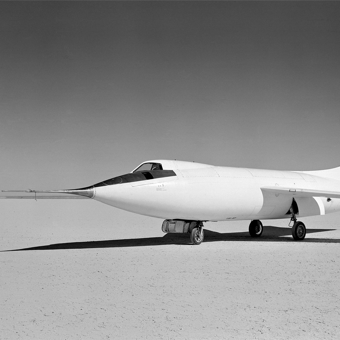 A vintage photo capturing the sleek, white D-558-II Skyrocket Aircraft from the X Planes series, an iconic piece of aviation history. This supersonic experimental aircraft features a pointed nose and delta wings, positioned on a flat, barren surface with clear skies in the background.