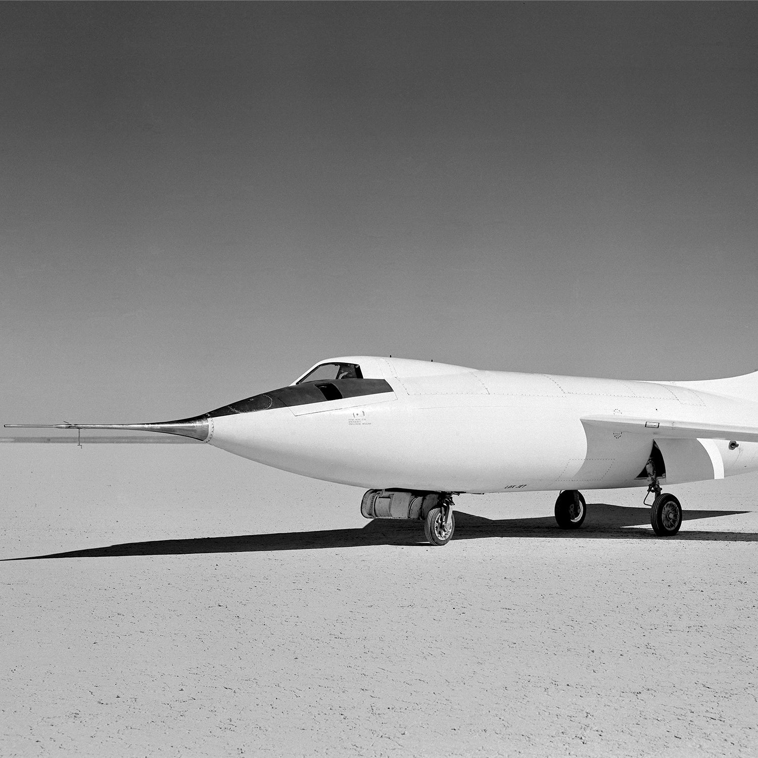 A vintage photo capturing the sleek, white D-558-II Skyrocket Aircraft from the X Planes series, an iconic piece of aviation history. This supersonic experimental aircraft features a pointed nose and delta wings, positioned on a flat, barren surface with clear skies in the background.