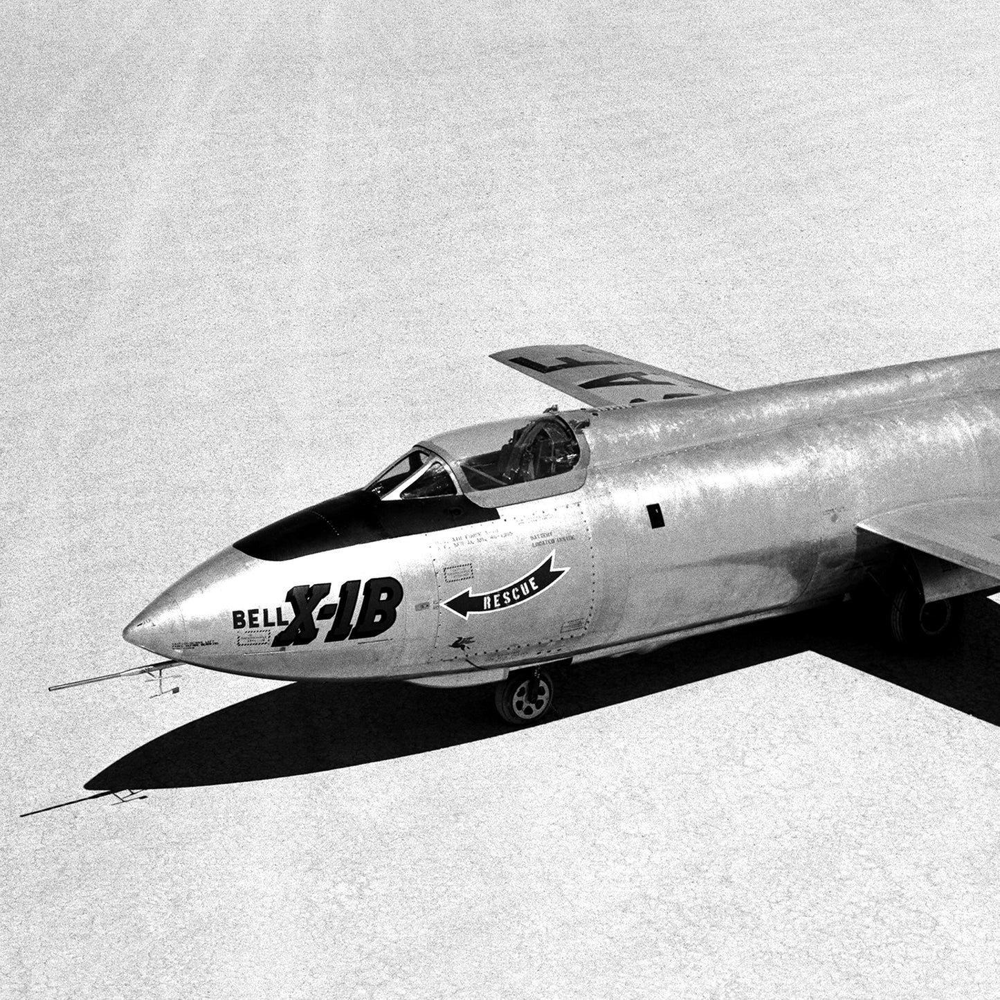 A black-and-white image of the "X-1B on Lakebed | X Planes" captures the sleek, streamlined design of the Bell X-1B aircraft, featuring "Bell X-1B" written near the cockpit along with a small arrow and the word "Republic." This iconic pioneer in aerospace history rests on a dry lake bed, embodying early supersonic flight ambitions.