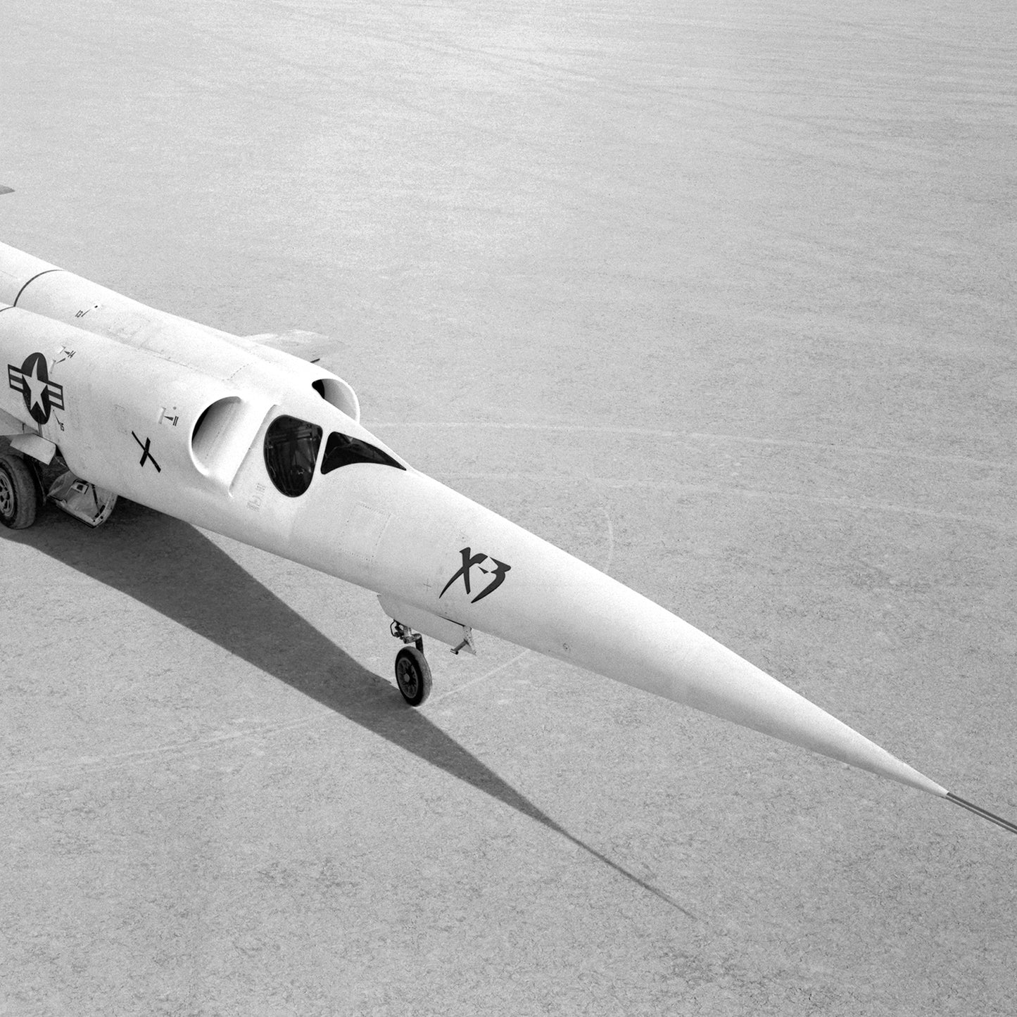 A black and white image captures the sleek, experimental X-3 aircraft designated as "X3." The fuselage is long and pointed, with a small undercarriage wheel visible. The aircraft features a minimalist design along with a US military star insignia on the side, making the X-3 Aircraft on Lakebed Print from X Planes perfect aviation wall art for enthusiasts.