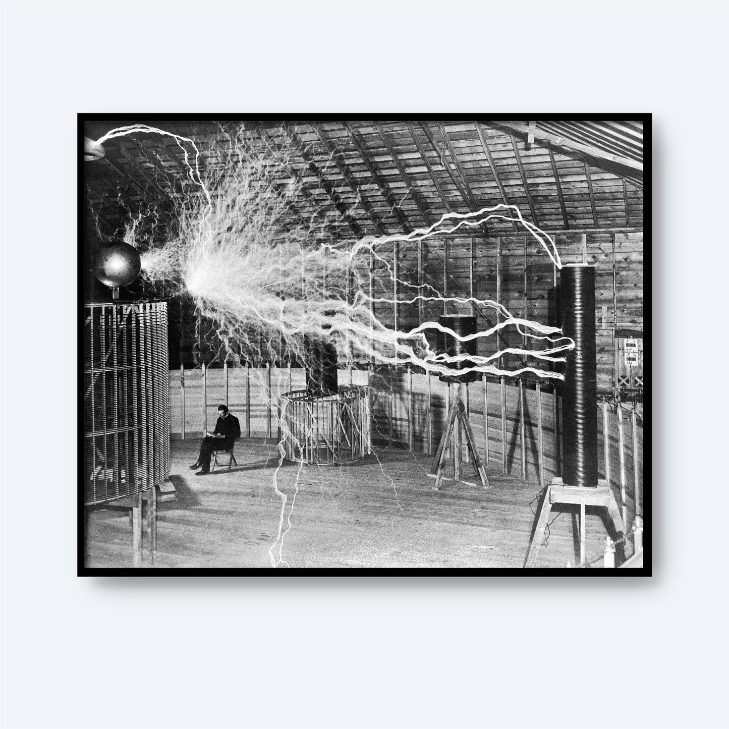 Description: Black and white image of an expansive indoor space with high ceilings emitting substantial electrical sparks. A figure, resembling Dr. Nikola Tesla, is seated in the background amidst electrical apparatuses generating the sparks. The scene captures an early 20th-century electrical experiment.

Product Name: Dr. Nikola Tesla in Laboratory Print