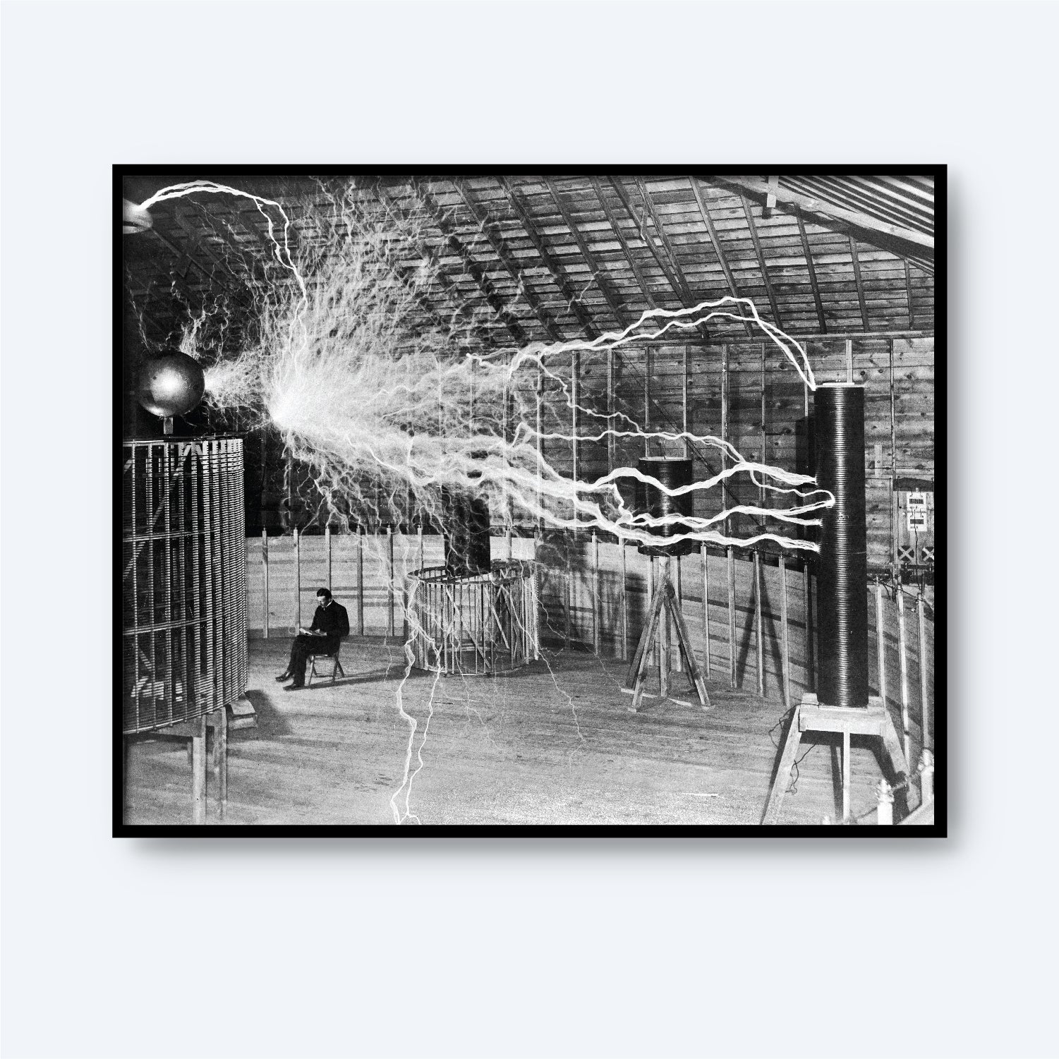 Description: Black and white image of an expansive indoor space with high ceilings emitting substantial electrical sparks. A figure, resembling Dr. Nikola Tesla, is seated in the background amidst electrical apparatuses generating the sparks. The scene captures an early 20th-century electrical experiment.

Product Name: Dr. Nikola Tesla in Laboratory Print
