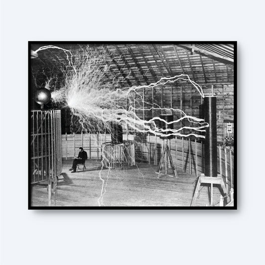 Description: Black and white image of an expansive indoor space with high ceilings emitting substantial electrical sparks. A figure, resembling Dr. Nikola Tesla, is seated in the background amidst electrical apparatuses generating the sparks. The scene captures an early 20th-century electrical experiment.

Product Name: Dr. Nikola Tesla in Laboratory Print