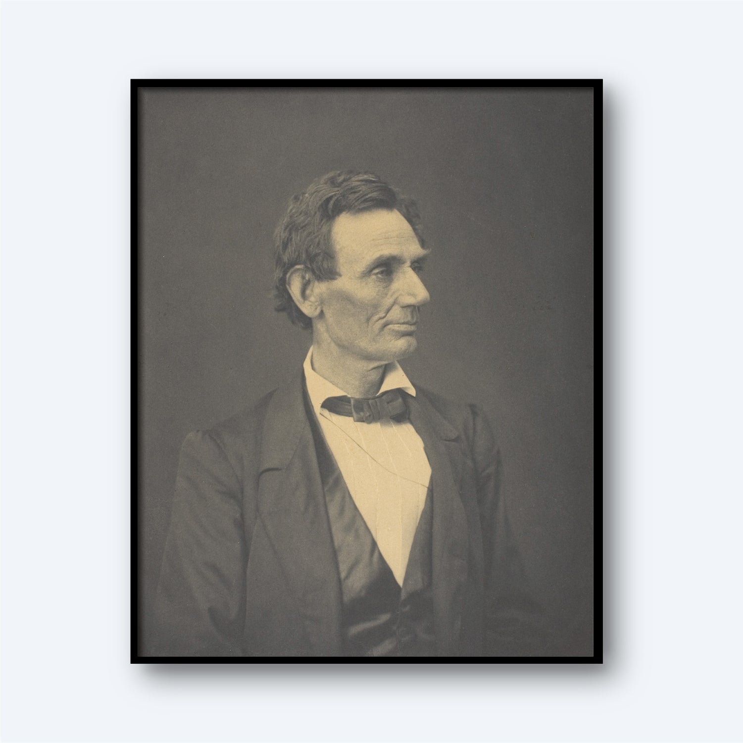 The "Abraham Lincoln by Alexander Hesler" photograph features a black-and-white portrait of a man with short, dark hair, dressed in a suit with a bow tie. He faces slightly to the left with a thoughtful expression. The portrait, distinguished by its gravitas akin to an Abraham Lincoln portrayal, is framed in black and set against a neutral background.
