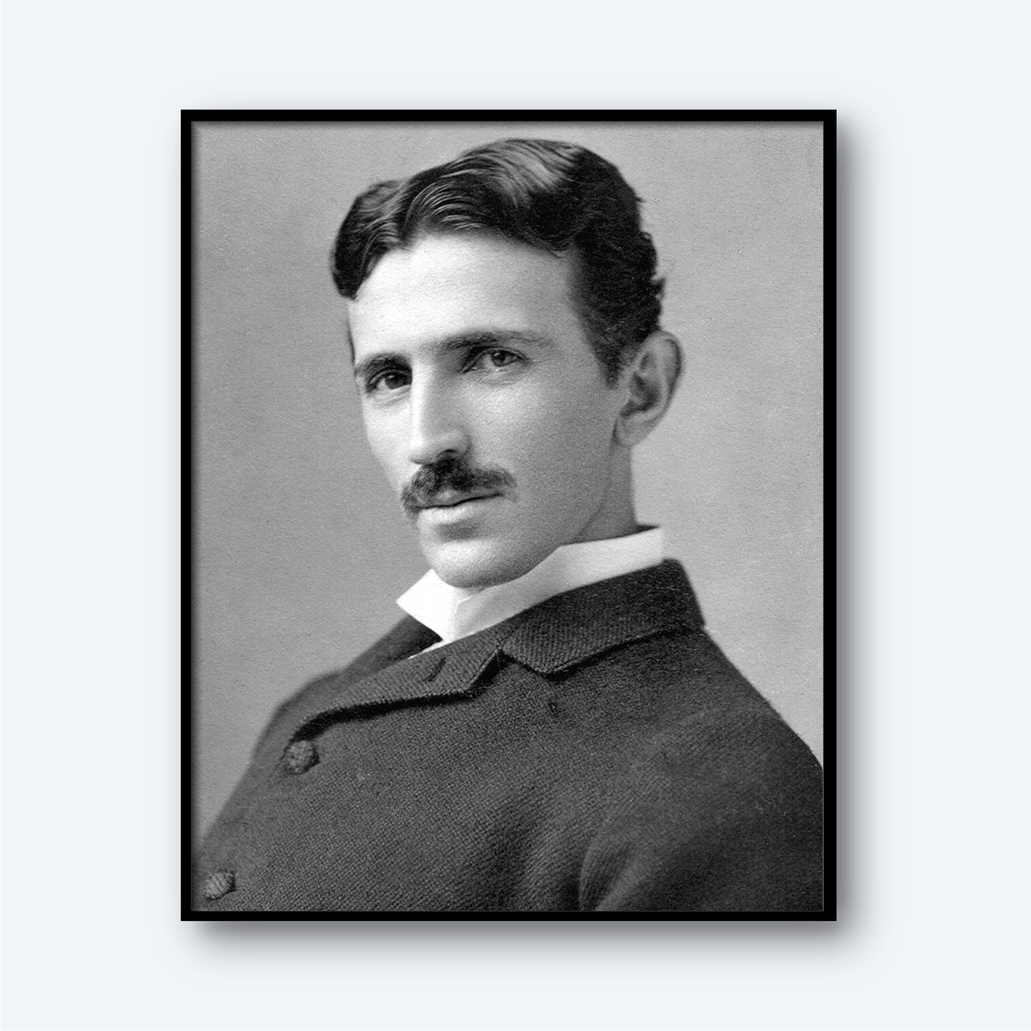 The Nikola Tesla Print features a black-and-white portrait of Tesla with wavy dark hair and a mustache, dressed in a suit with a white collar. He is turned slightly to the side and gazes directly at the camera with a serious expression. The neutral, light gray background enhances the image, reflecting his era of modern electricity.