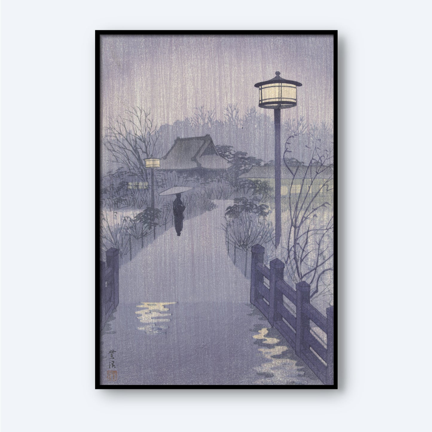 The framed "Rainy Night at Shinobazu Pond" artwork by Kasamatsu Shiro depicts a serene, rainy evening where a person with an umbrella walks along a path lined with street lamps and bordered by a wooden fence. In the background, trees and a house are visible, all enveloped in a gentle, misty ambiance.