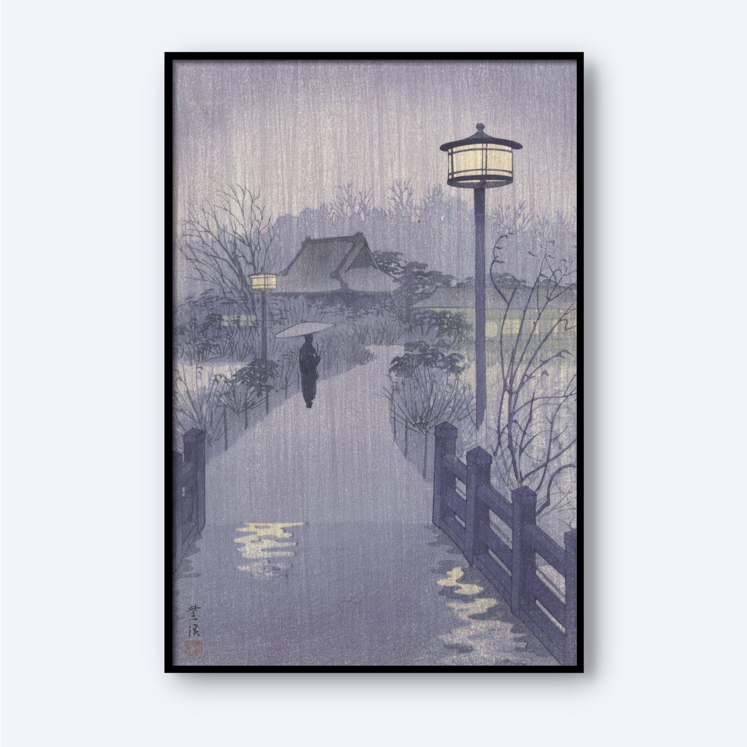 The framed "Rainy Night at Shinobazu Pond" artwork by Kasamatsu Shiro depicts a serene, rainy evening where a person with an umbrella walks along a path lined with street lamps and bordered by a wooden fence. In the background, trees and a house are visible, all enveloped in a gentle, misty ambiance.