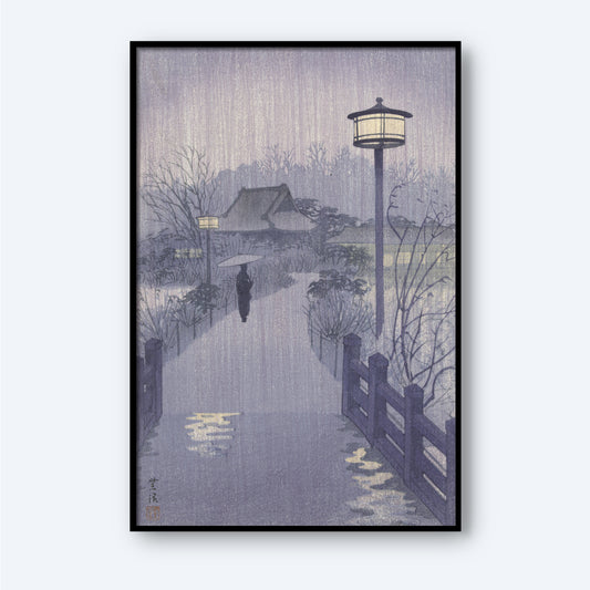 The framed "Rainy Night at Shinobazu Pond" artwork by Kasamatsu Shiro depicts a serene, rainy evening where a person with an umbrella walks along a path lined with street lamps and bordered by a wooden fence. In the background, trees and a house are visible, all enveloped in a gentle, misty ambiance.