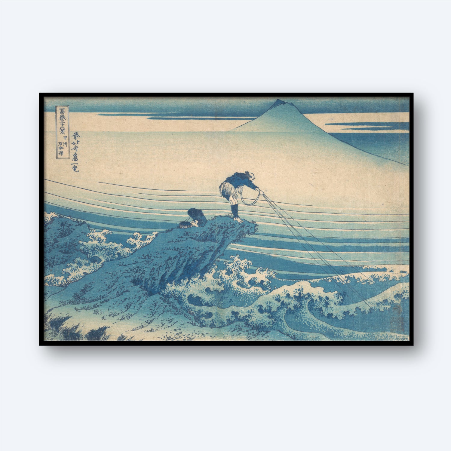 The framed traditional Japanese woodblock print "Kajikazawa in Kai Province by Katsushika Hokusai" captures two fishermen on a rocky coastline against a turbulent ocean. One man stands, pulling on fishing lines, while the other crouches. As part of Hokusai's "Thirty-Six Views of Mount Fuji," this piece features the mountain under a clear sky.