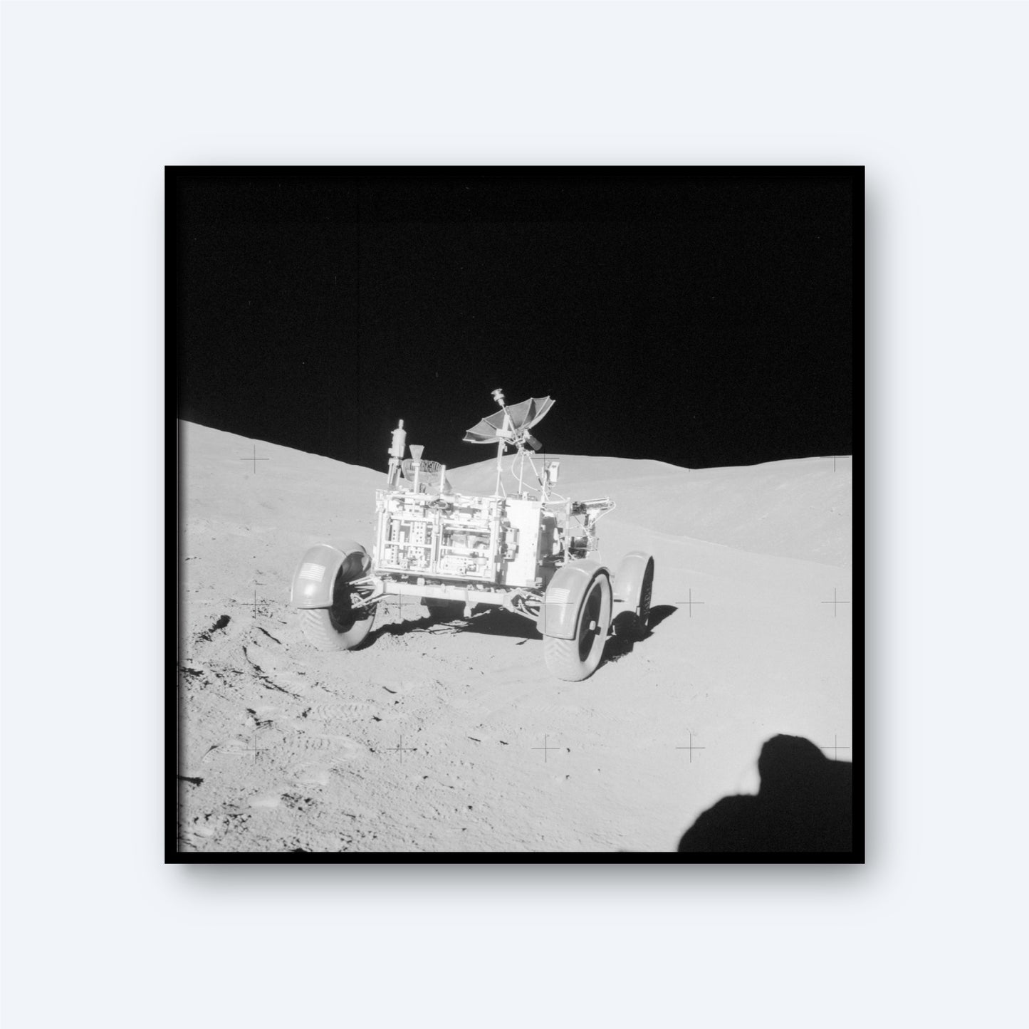 A black and white image of the NASA Apollo Lunar Rover on the moon's surface. The rover's wheels and equipment are visible, positioned on slightly uneven terrain. The background shows the stark, shadowed landscape of the moon, with a dark sky above, evoking the vastness of space and intricate details of astronomy.