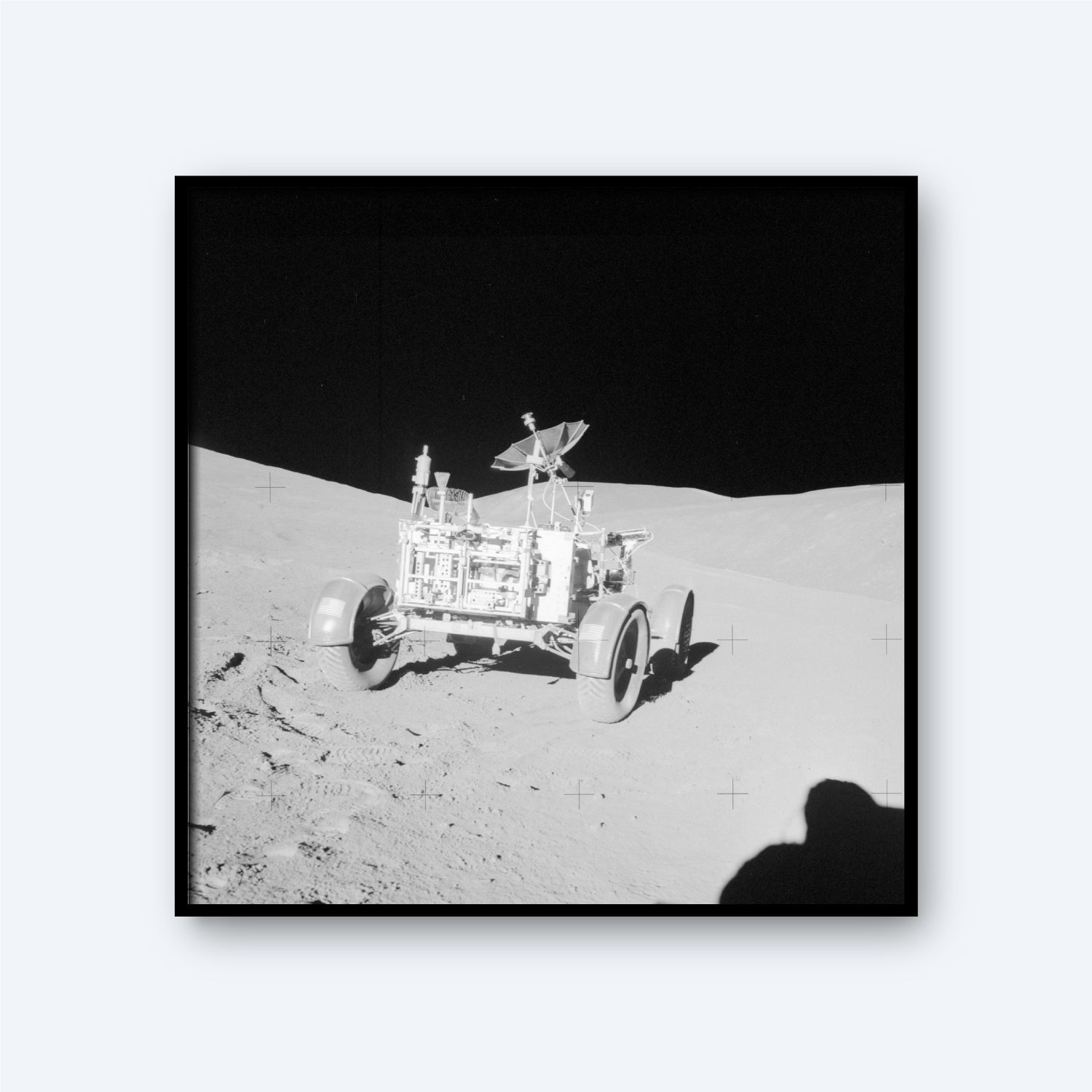 A black and white image of the NASA Apollo Lunar Rover on the moon's surface. The rover's wheels and equipment are visible, positioned on slightly uneven terrain. The background shows the stark, shadowed landscape of the moon, with a dark sky above, evoking the vastness of space and intricate details of astronomy.