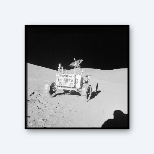 A black and white image of the NASA Apollo Lunar Rover on the moon's surface. The rover's wheels and equipment are visible, positioned on slightly uneven terrain. The background shows the stark, shadowed landscape of the moon, with a dark sky above, evoking the vastness of space and intricate details of astronomy.
