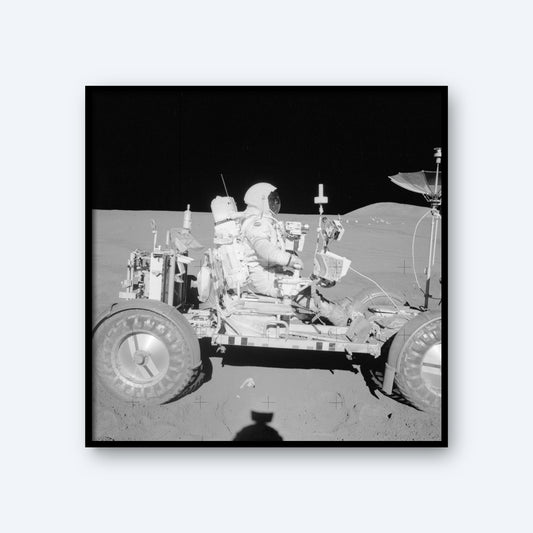The NASA Apollo 15 Astronaut in the Lunar Rover on The Moon features an astronaut in a spacesuit seated on the Lunar Rover against the backdrop of the lunar landscape, capturing an iconic moment in space history. The rover is equipped with various instruments and antennas, with the shadow of the photographer visible in the foreground.