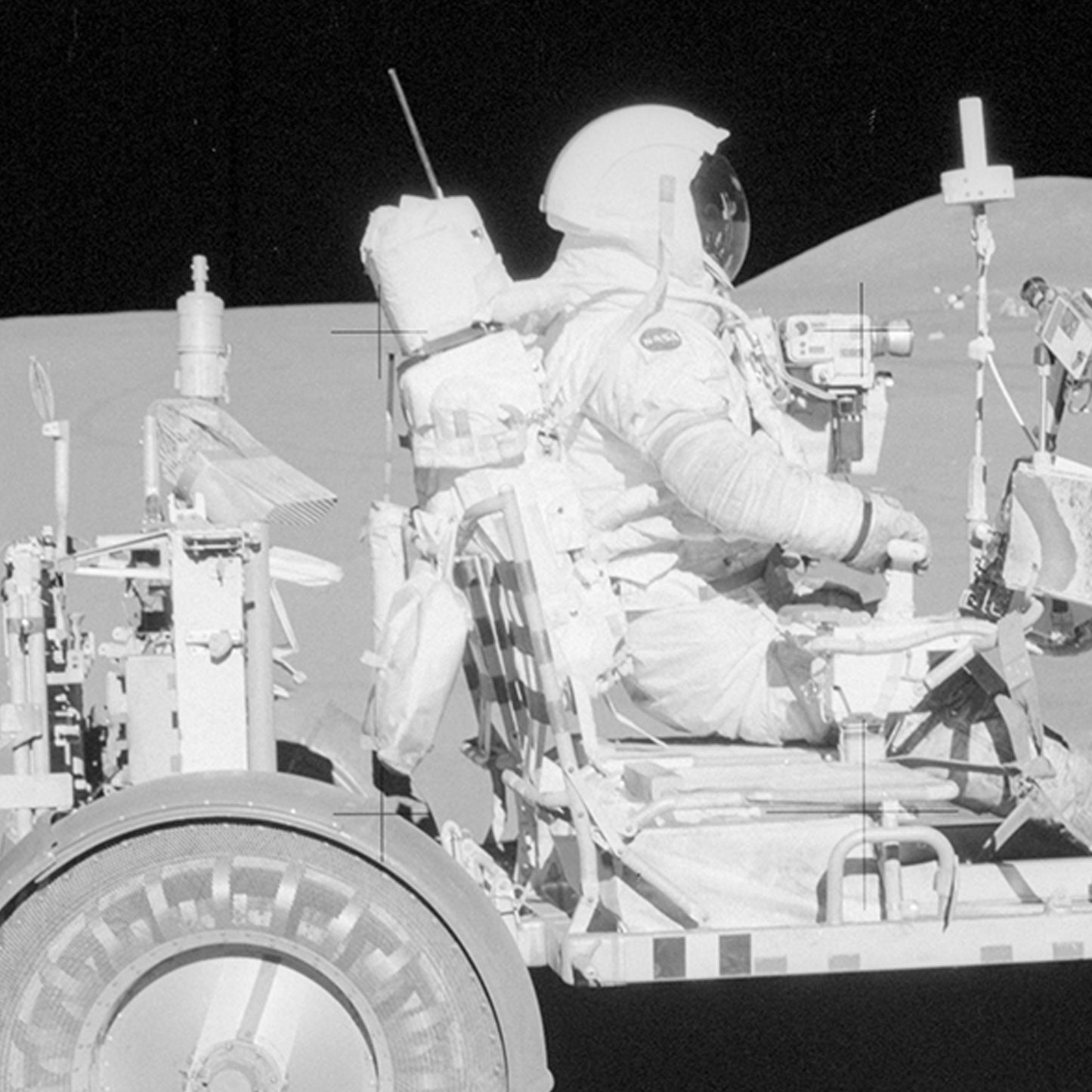 NASA Apollo 15 Astronaut David R. Scott sits in the driver's seat of the Lunar Roving Vehicle on the Moon's surface. The vehicle, equipped with scientific instruments and equipment, stands out against the barren lunar landscape, with the horizon stretching into space in the background.