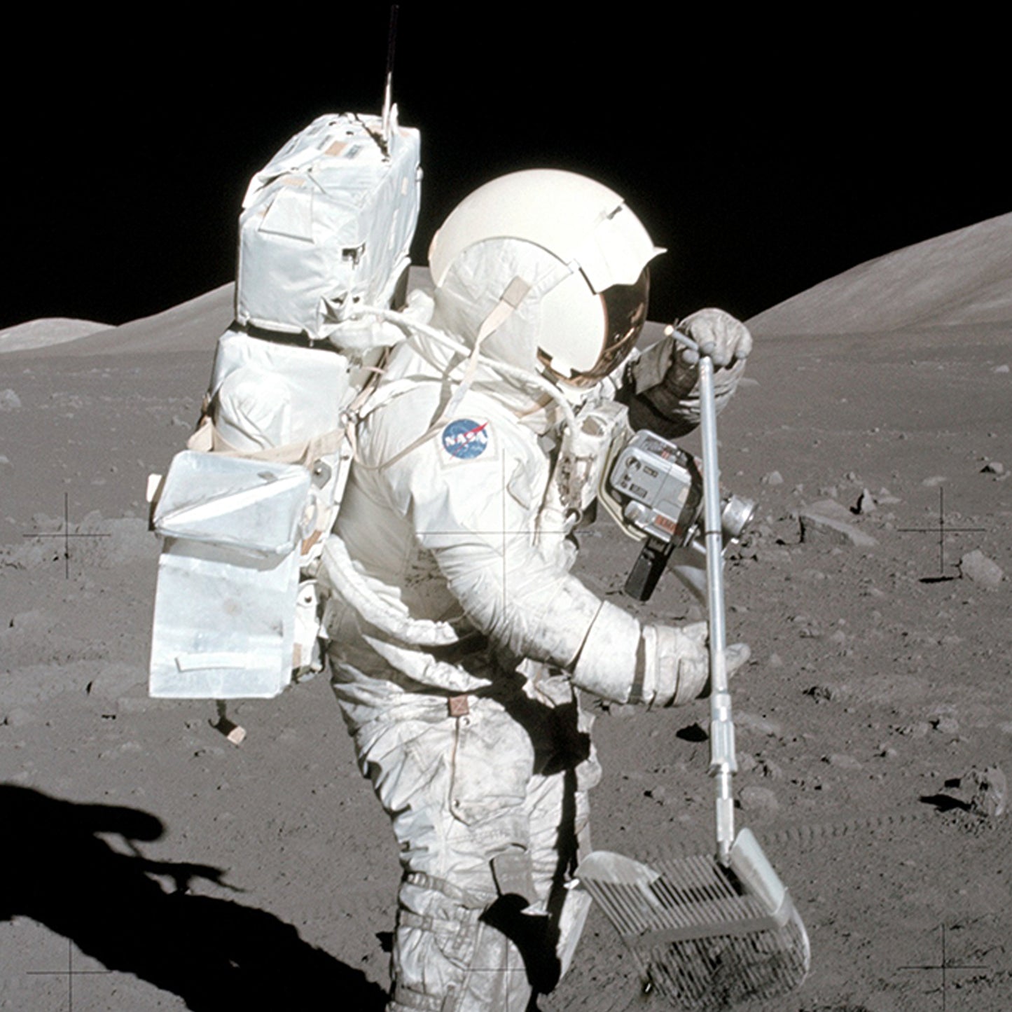 The NASA Apollo 17 astronaut, adorned in a white spacesuit and helmet featuring a reflective visor and the iconic NASA logo, uses a tool to collect samples on the lunar surface. With a large backpack on their back, they stand against the moon's barren, rocky terrain and the boundless stretch of space in the background.
