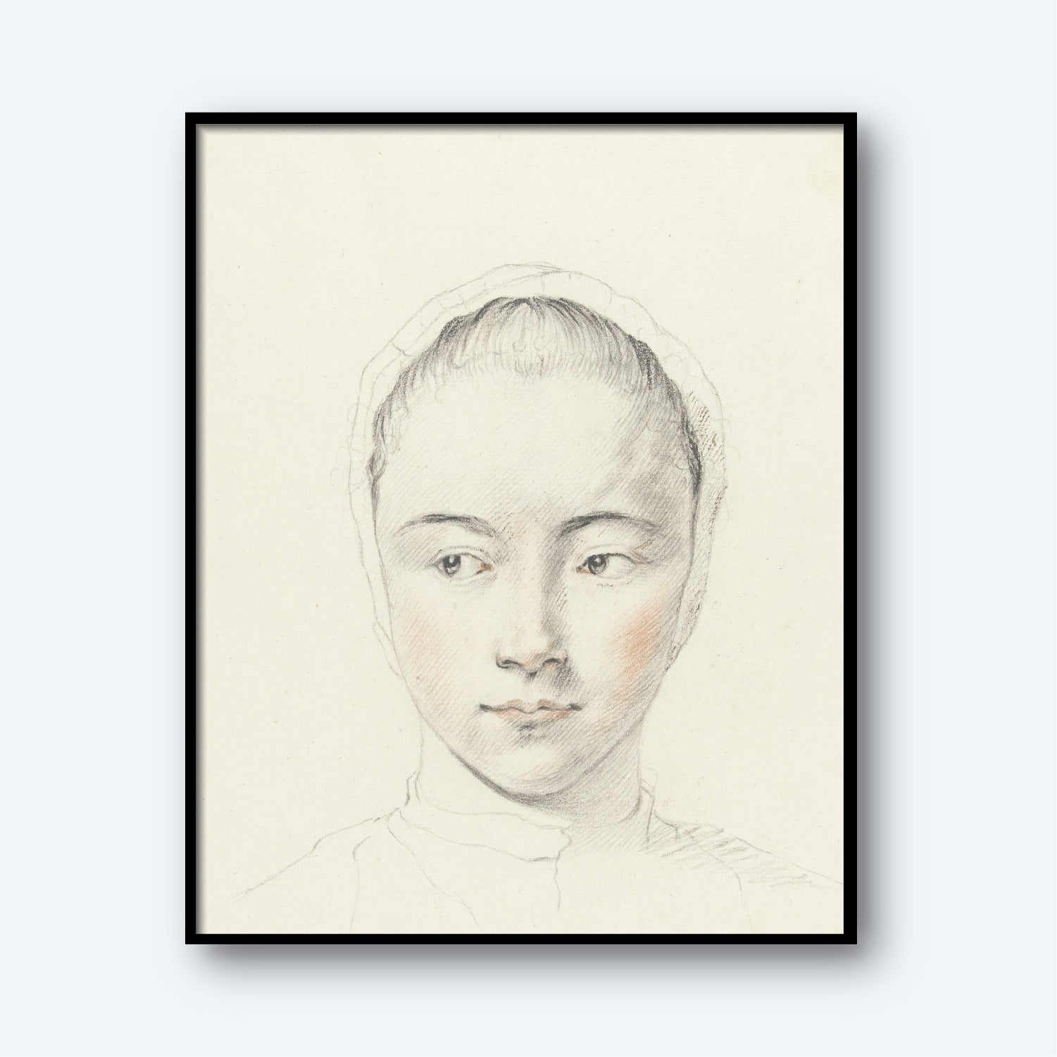 A framed sketch of a young woman with a serene expression. This delicate pencil portrait, titled *Kop van een meisje by Judith M. Testart,* features slight touches of color highlighting her cheeks. She wears a headscarf, and the plain white background makes her the focal point of this exquisite wall art.