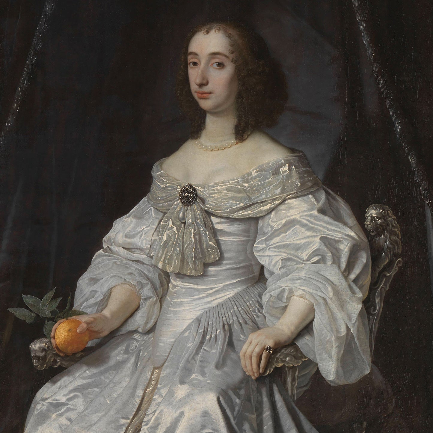 The painting titled "Mary Stuart Princess of Orange" by Bartholomeus van der Helst from the Dutch Golden Age portrays Mary Stuart with curly hair, seated on an ornately carved chair. She is dressed in an elaborate white gown adorned with a brooch and a pearl necklace. Her right hand holds an orange with green leaves, while her left hand rests on her lap, displaying a ring.