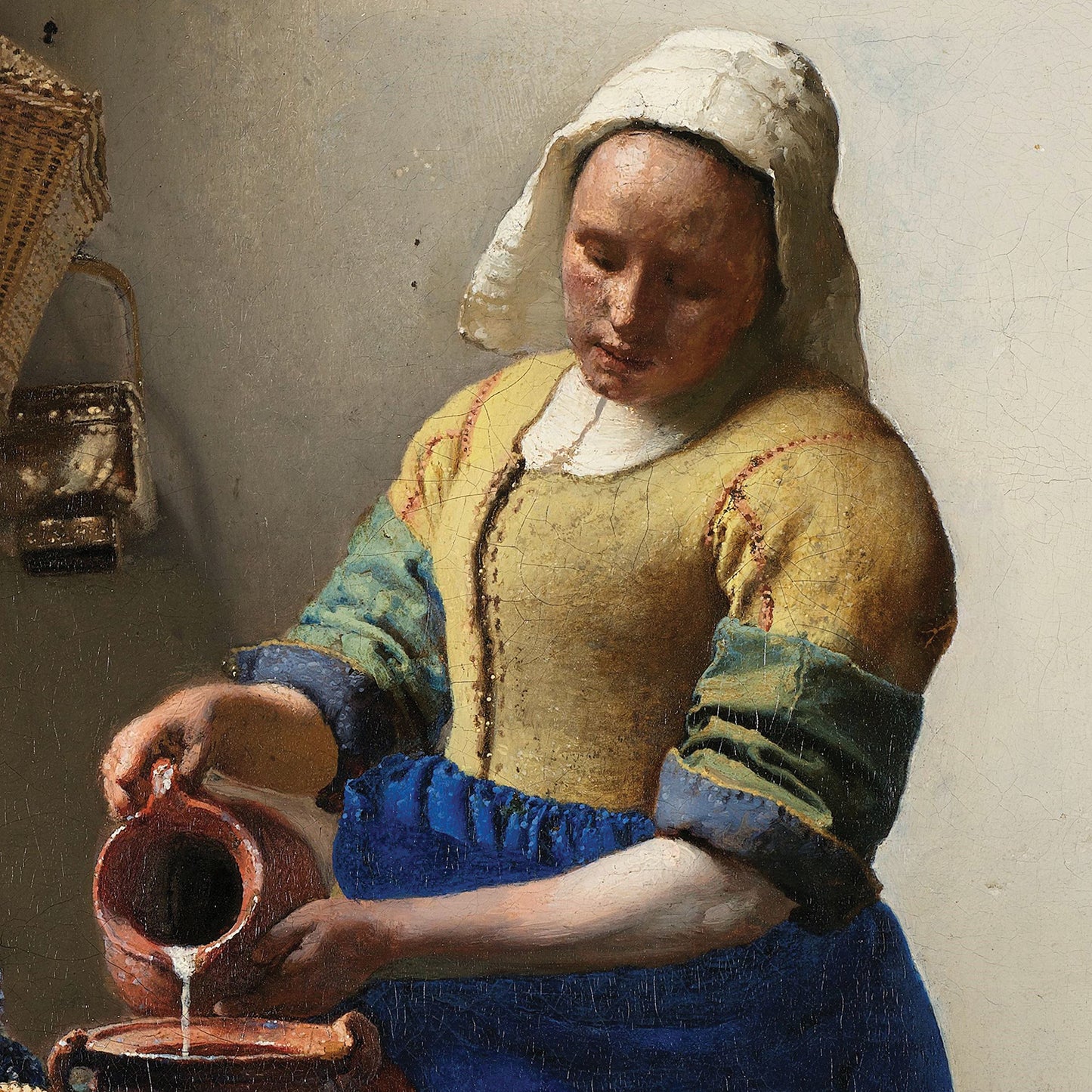 The Milkmaid by Johannes Vermeer depicts a woman in a white headscarf, yellow bodice, blue apron, and green-and-blue sleeves, pouring milk from a red jug into a bowl held by her left hand. In the background, a basket and loaf of bread are visible, highlighting the Dutch Golden Age style characteristic of Vermeer's work.