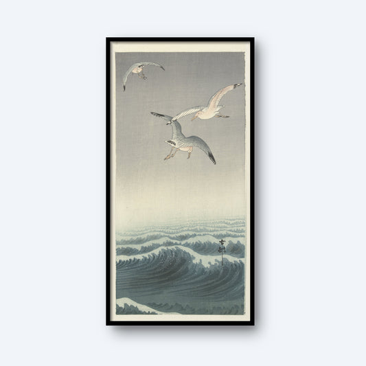 A framed "Three Seagulls by Ohara Koson | Vintage Japanese Woodblock Print" features three seagulls soaring above a turbulent ocean with rolling waves. The scene is illustrated in a traditional Japanese ukiyo-e style, reminiscent of Ohara Koson's work, with soft hues of blue and gray dominating the composition.