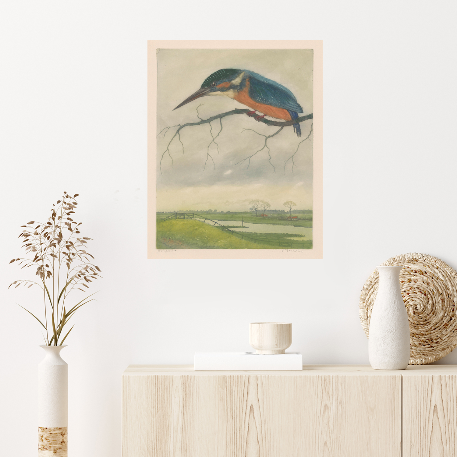 A minimalist room features a wooden sideboard adorned with a ceramic vase, dried grasses, and a wicker decoration. Above the sideboard hangs a vintage wildlife art piece—a framed Kingfisher by Frans Everbag | Vintage Print, depicting a kingfisher bird perched on a branch, overlooking a scenic green countryside landscape.