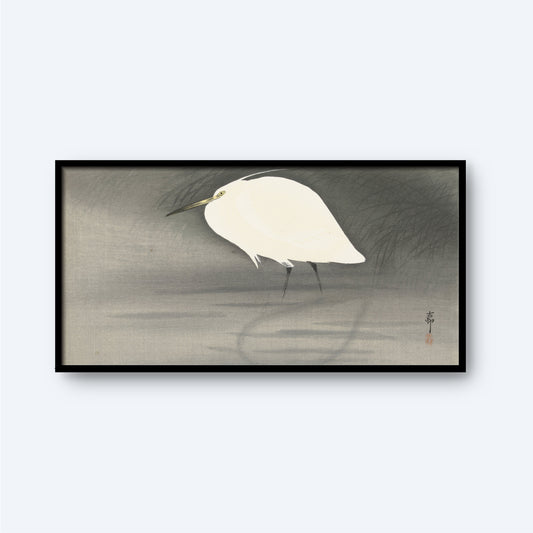 A minimalistic painting titled "Egret In Swamp Waiting for Fish" by Ohara Koson, features a white egret with a slender neck and long legs standing gracefully in shallow water. The scene is reminiscent of traditional Japanese prints, set against a background of muted, soft hues of gray and green that evoke the feeling of fog or mist. The serene composition is elegantly framed in a simple black frame.